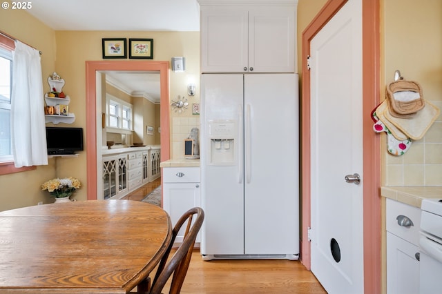 kitchen with backsplash, white refrigerator with ice dispenser, tile counters, and white cabinetry