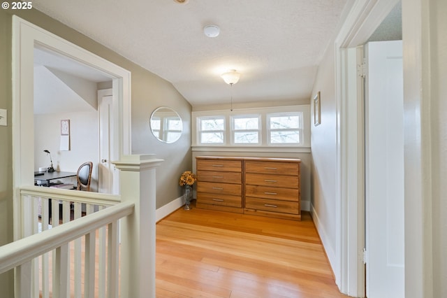 hall featuring light wood-style flooring, a textured ceiling, and baseboards