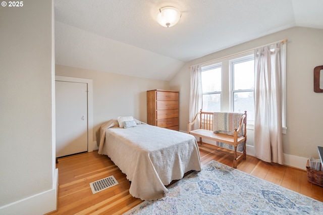 bedroom featuring visible vents, wood-type flooring, baseboards, and vaulted ceiling