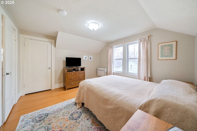 bedroom with vaulted ceiling, baseboards, light wood finished floors, and a textured ceiling