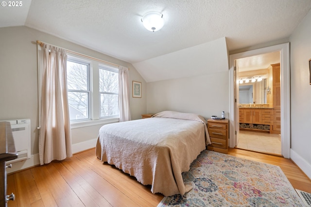 bedroom featuring a textured ceiling, vaulted ceiling, and light wood finished floors