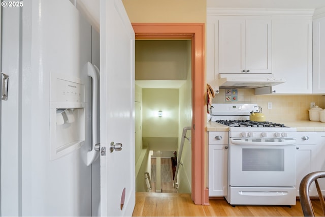 kitchen featuring backsplash, white gas stove, under cabinet range hood, tile countertops, and white cabinets