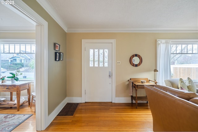 entrance foyer with visible vents, baseboards, crown molding, and light wood-style floors