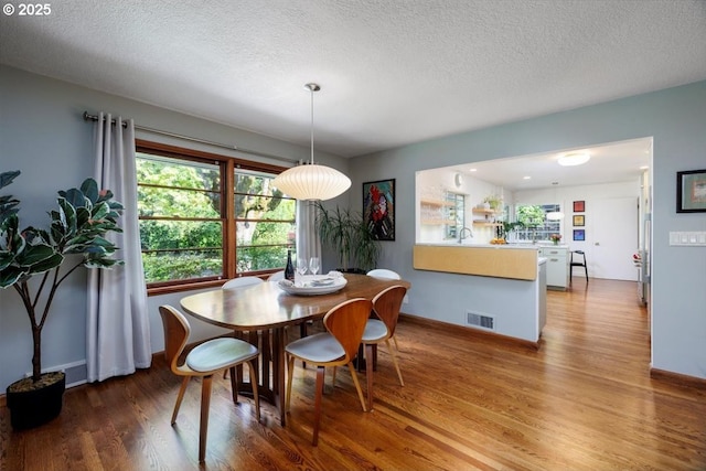 dining space with visible vents, baseboards, a textured ceiling, and wood finished floors