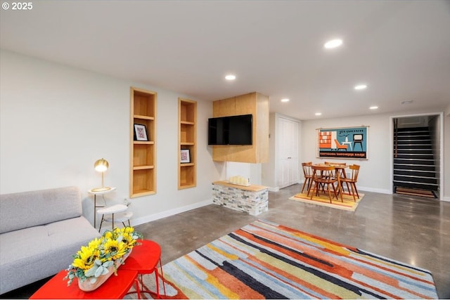 living area featuring built in features, baseboards, concrete floors, and stairs
