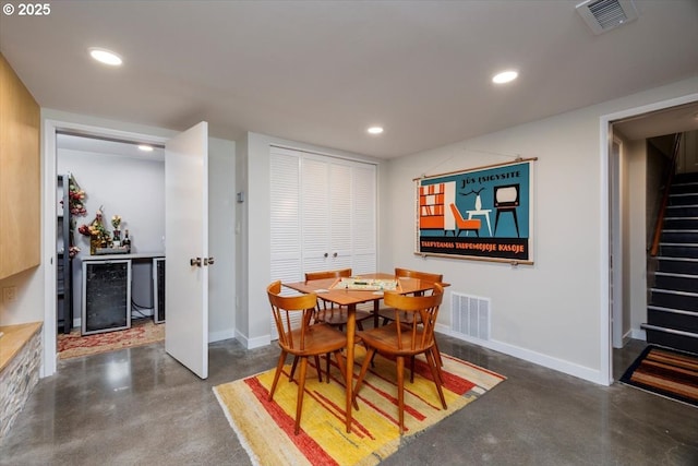 dining space with finished concrete floors, visible vents, baseboards, beverage cooler, and stairs