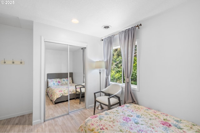 bedroom with baseboards, visible vents, wood finished floors, a textured ceiling, and a closet