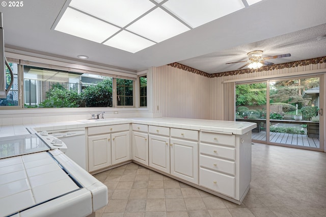 7785 SW Fairway Dr, Wilsonville, OR 97070 - kitchen featuring tile countertops, a peninsula, a sink, ceiling fan, and white cabinetry