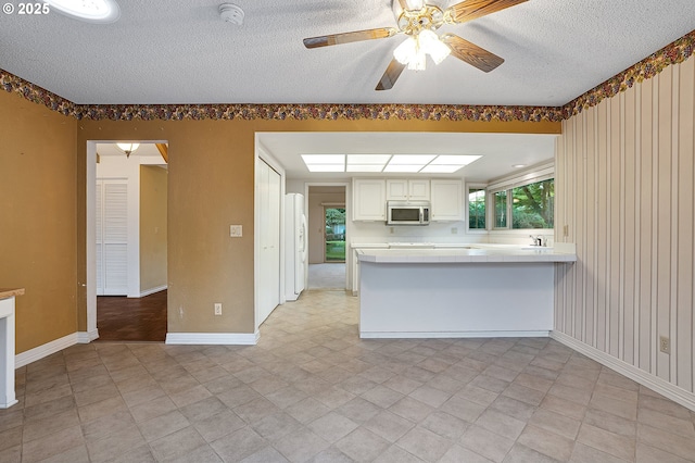 7785 SW Fairway Dr, Wilsonville, OR 97070 - kitchen with stainless steel microwave, white refrigerator with ice dispenser, a peninsula, a textured ceiling, and tile countertops