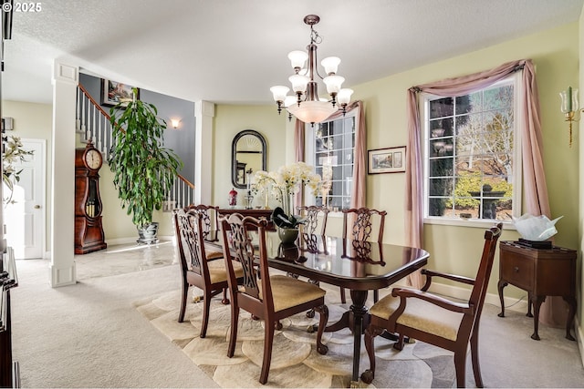 carpeted dining area featuring a textured ceiling, a chandelier, and ornate columns