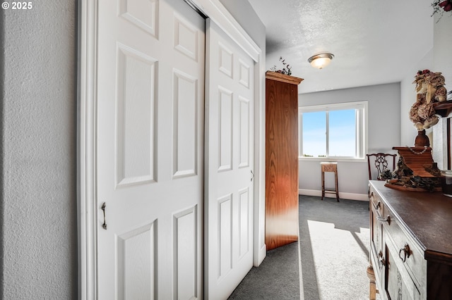 hallway with dark carpet and a textured ceiling