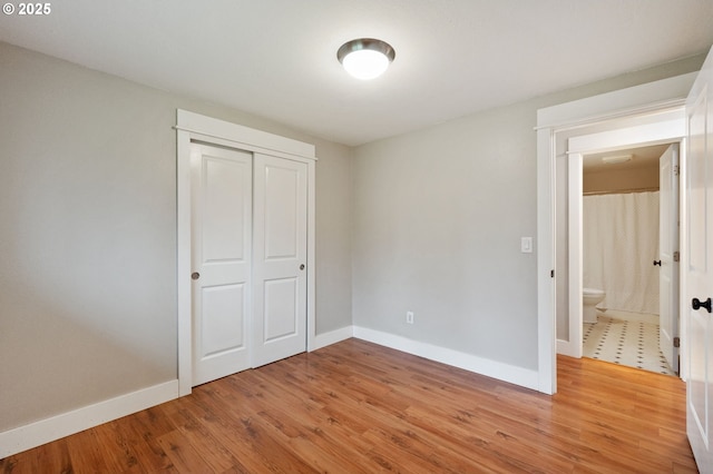 unfurnished bedroom featuring light wood-type flooring, a closet, and ensuite bathroom