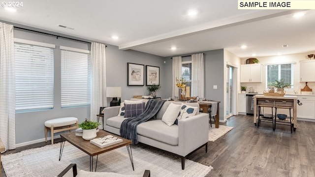 living area with dark wood-style floors, a healthy amount of sunlight, beamed ceiling, and baseboards