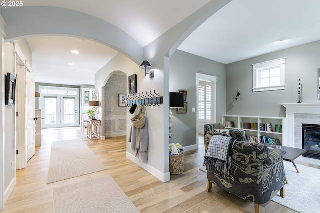 interior space with arched walkways, recessed lighting, baseboards, light wood-style floors, and a glass covered fireplace