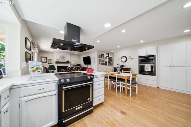 11820 SW Reid Ct, Beaverton, OR 97008 - kitchen with wall chimney range hood, range with electric stovetop, light wood-type flooring, white cabinets, and a peninsula