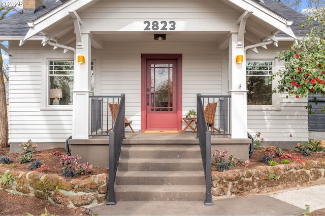 doorway to property featuring covered porch, roof with shingles, and a chimney