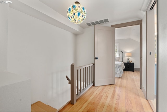 hallway featuring an upstairs landing, visible vents, light wood-style floors, and vaulted ceiling