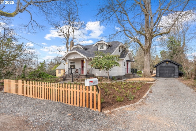 view of front of home featuring an outbuilding, a fenced front yard, a detached garage, gravel driveway, and a chimney