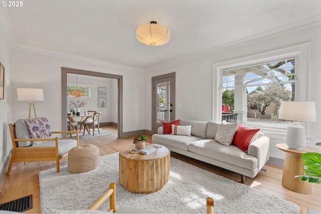 living area with visible vents, wood finished floors, baseboards, and ornamental molding