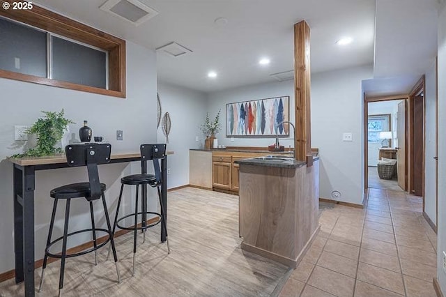 kitchen featuring dark countertops, a peninsula, baseboards, and a sink