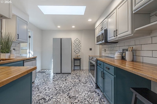 kitchen with blue cabinets, a skylight, butcher block counters, and appliances with stainless steel finishes