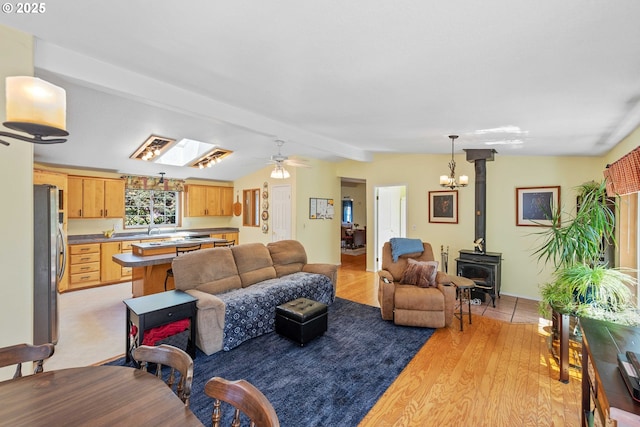 living room featuring a wood stove, light wood-style floors, lofted ceiling, and ceiling fan with notable chandelier