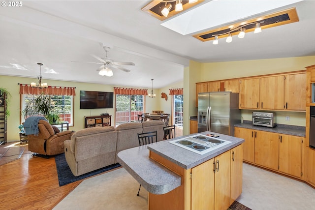 kitchen with white electric stovetop, a center island, dark countertops, vaulted ceiling with skylight, and stainless steel fridge with ice dispenser