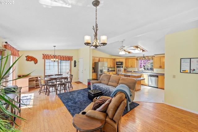 living area featuring vaulted ceiling, light wood-style flooring, ceiling fan with notable chandelier, and baseboards
