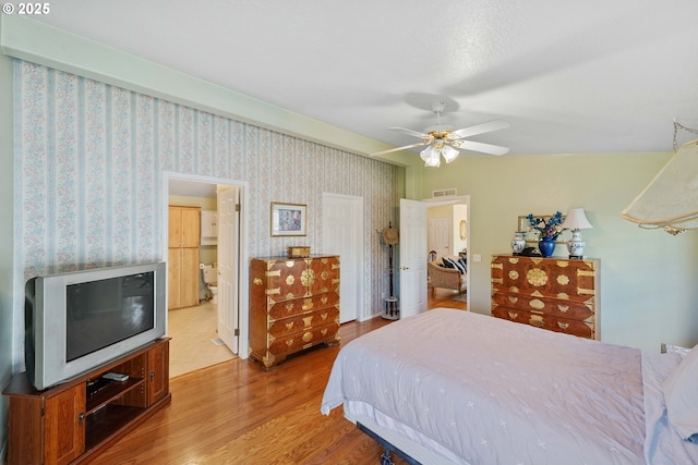 bedroom with ceiling fan, visible vents, wallpapered walls, and wood finished floors