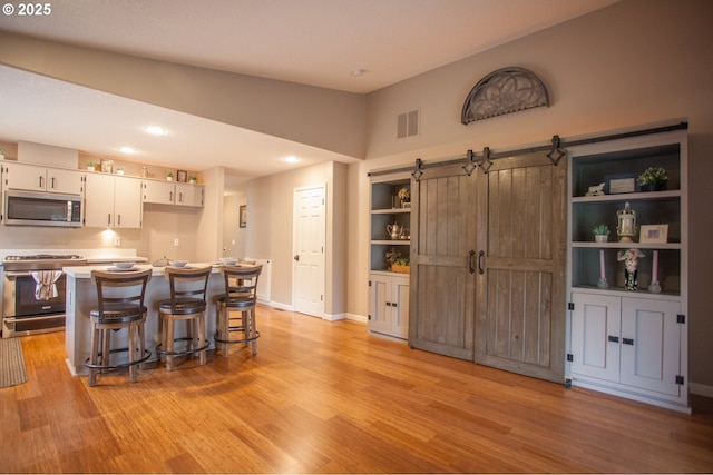 kitchen featuring a breakfast bar, light wood-type flooring, a barn door, white cabinets, and appliances with stainless steel finishes