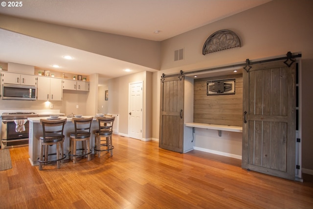 kitchen featuring stainless steel appliances, high vaulted ceiling, a barn door, and white cabinets