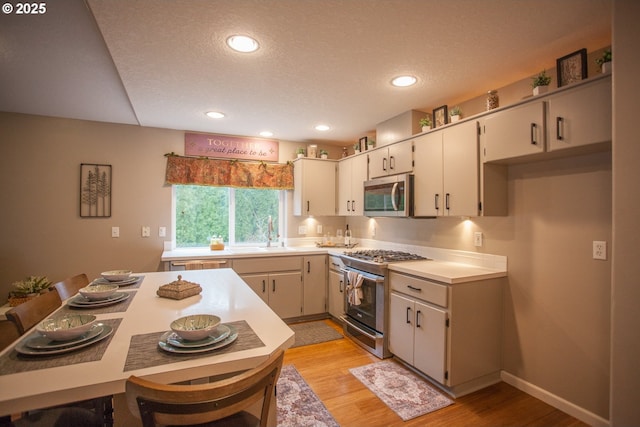 kitchen with white cabinets, a textured ceiling, light wood-type flooring, and appliances with stainless steel finishes