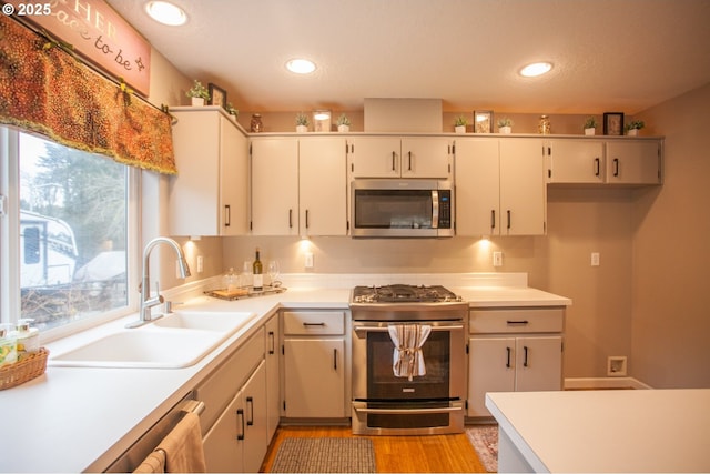 kitchen featuring stainless steel appliances, white cabinetry, sink, and light hardwood / wood-style flooring