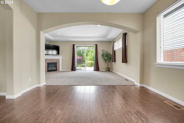 20021 Tharp Ct, Oregon City, OR 97045 - unfurnished living room featuring arched walkways, dark wood-style floors, a tiled fireplace, and a tray ceiling