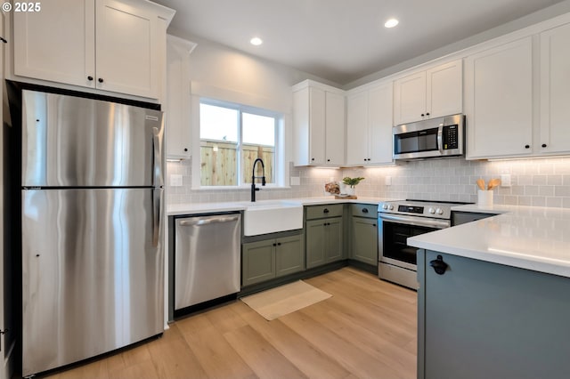 7265 SE Duke St Unit 2, Portland, OR 97206 - kitchen with appliances with stainless steel finishes, light wood finished floors, backsplash, white cabinets, and recessed lighting