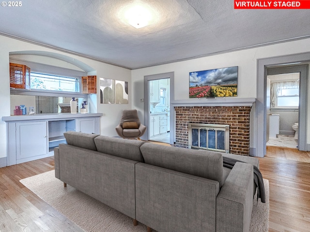 living area featuring a textured ceiling, wood finished floors, crown molding, and a brick fireplace