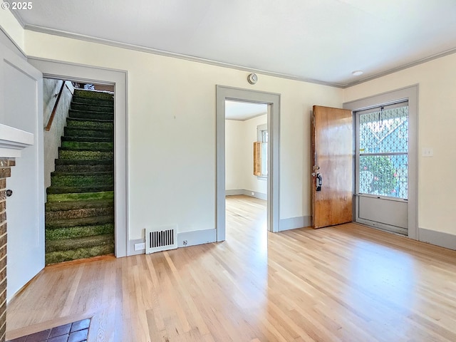 interior space featuring light wood finished floors, visible vents, crown molding, baseboards, and stairway