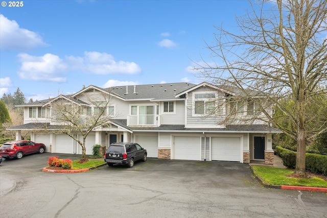 view of front facade featuring driveway, stone siding, roof with shingles, and an attached garage