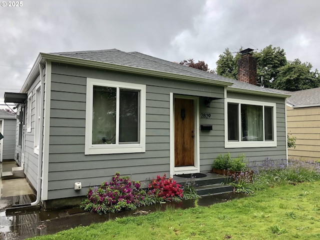 bungalow with a front lawn, a chimney, and roof with shingles