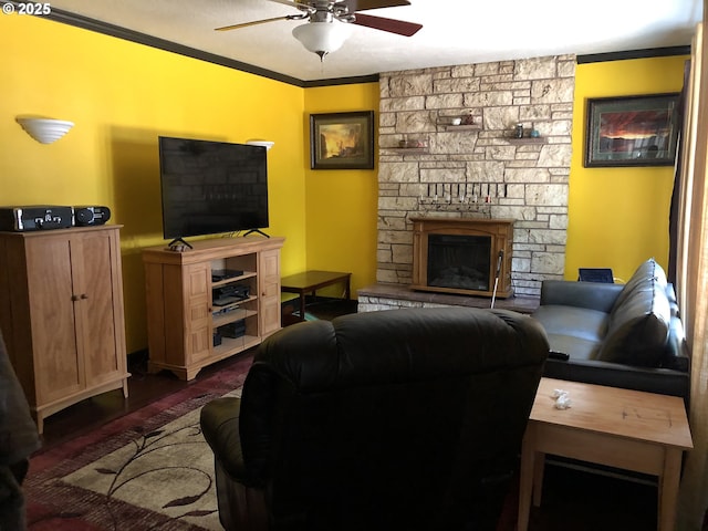 living room featuring dark wood finished floors, a stone fireplace, ornamental molding, and ceiling fan