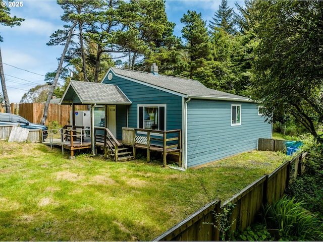 back of property with a fenced backyard, a wooden deck, a shingled roof, and a lawn
