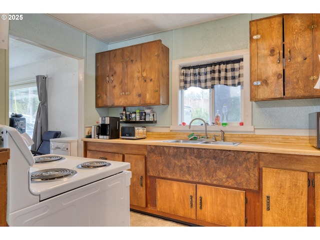 kitchen with white electric range oven, brown cabinetry, a sink, and a healthy amount of sunlight