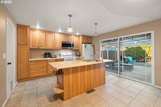 kitchen featuring sink, white appliances, a kitchen island with sink, light tile patterned flooring, and decorative light fixtures