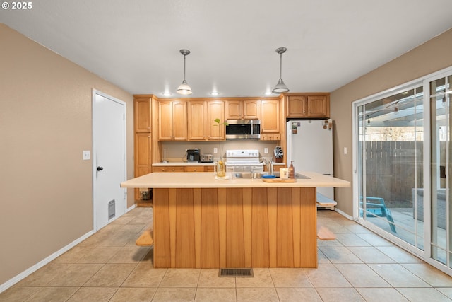 kitchen featuring pendant lighting, light tile patterned floors, white appliances, and an island with sink