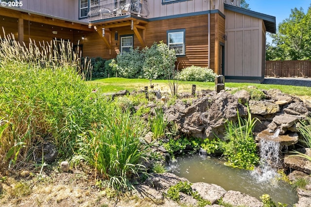 view of yard featuring a small pond, fence, and a balcony