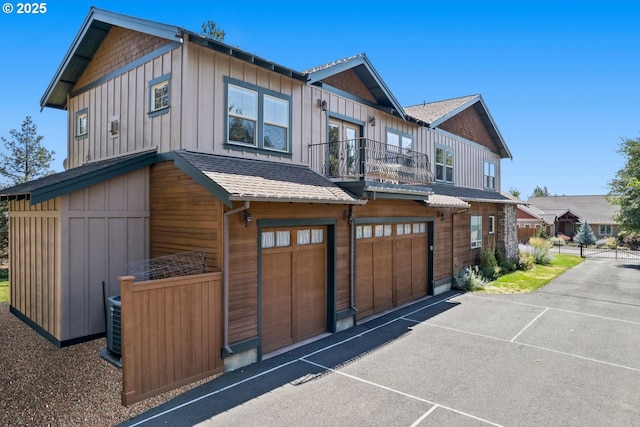 view of front facade featuring roof with shingles, a garage, board and batten siding, a balcony, and driveway