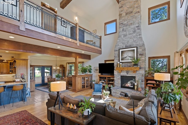 living area with a towering ceiling, beam ceiling, a stone fireplace, light wood-style floors, and a notable chandelier