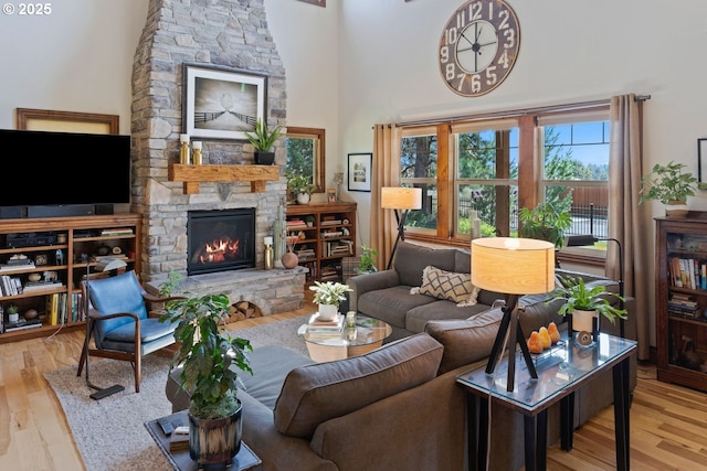 living area featuring a high ceiling, a stone fireplace, and wood finished floors