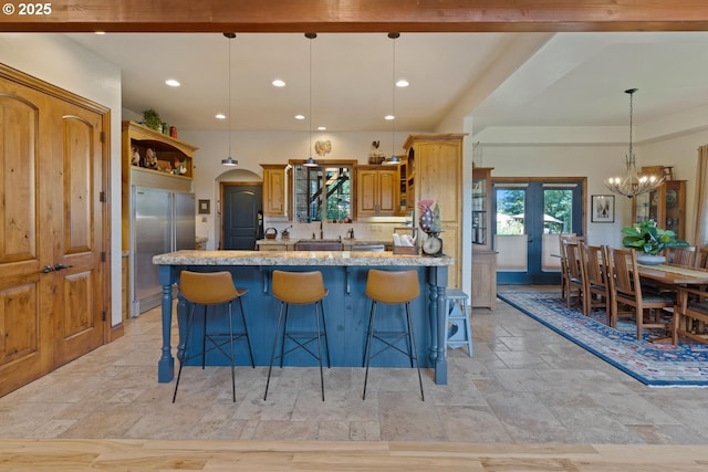 kitchen featuring open shelves, light stone counters, a chandelier, a kitchen bar, and built in refrigerator