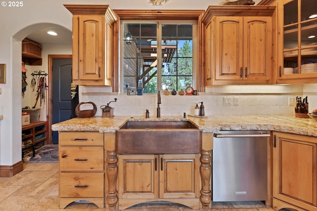 kitchen featuring glass insert cabinets, tasteful backsplash, light stone counters, a sink, and dishwasher
